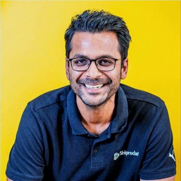 Professional man wearing glasses and a navy blue Shiprocket polo shirt smiling against a bright yellow background for corporate headshot photography.