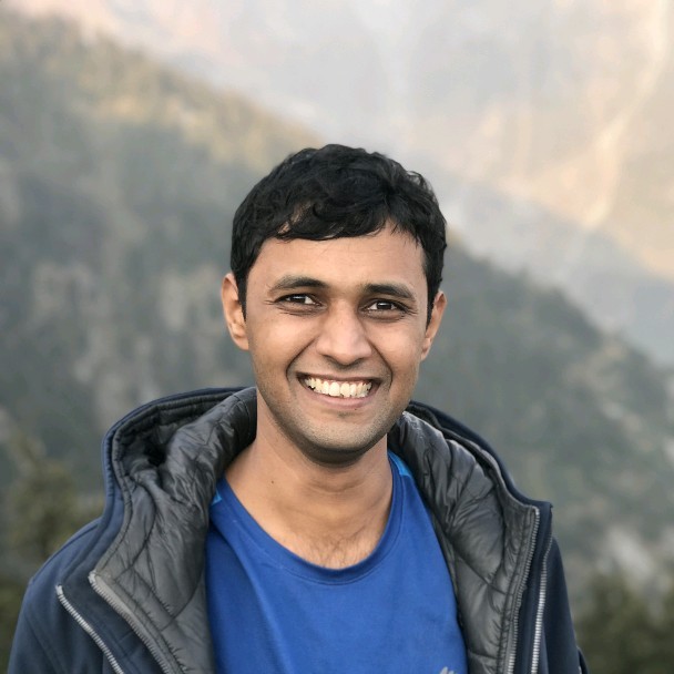 Young man smiling at camera wearing blue shirt and black jacket with misty mountain landscape background during outdoor adventure travel photography