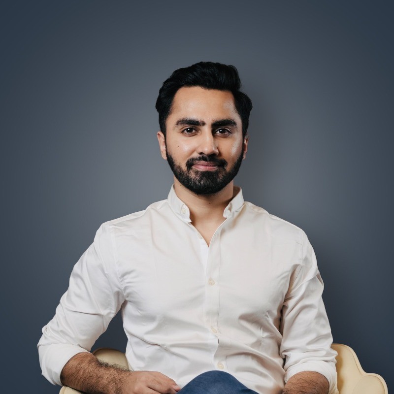 Professional headshot of a bearded man wearing a white button-up shirt seated against a neutral gray background for corporate or business portrait photography.